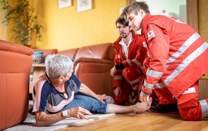 Rotkreuz-Sanitäter helfen einer Dame, nachdem sie auf ihrem Rufhillfe-Armband den Notrufknopf gedrückt hat.